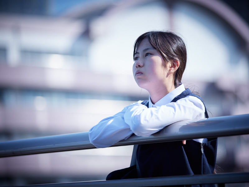手すりに寄りかかって、悲しそうな一人の中学生女子
